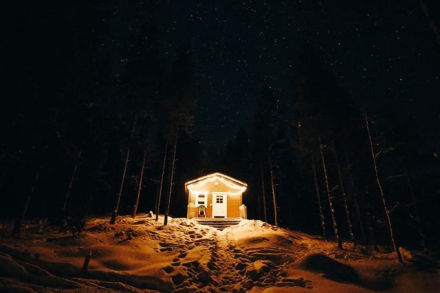 Beleuchtete schwedische Hütte im dunklen, verschneiten Wald